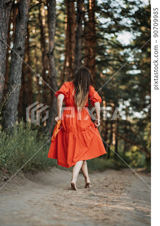 Barefoot happy young woman in red dress with hand raised dancing in pine forest at summer day. Barefoot happy young woman in red dress with hand raised dancing in pine forest at summer day. 90709985