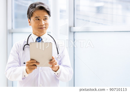 A doctor in a white coat standing with a tablet PC in the facility 90710113