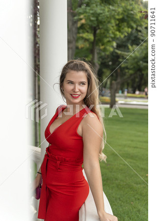 Charming blonde woman in red dress with deep neckline. Portrait of sexy young woman in summer park. 90711641