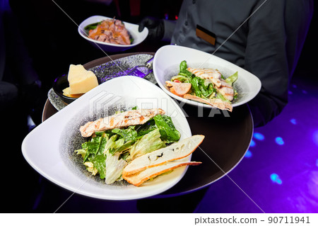 Waiter holding plates of Caesar salad with chicken breast and parmesan 90711941