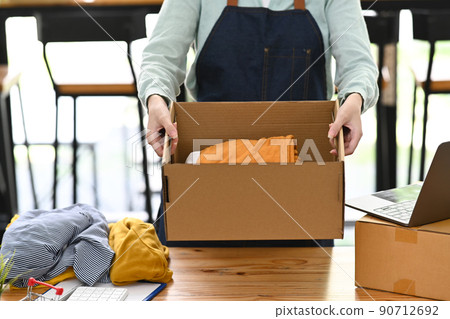 Cropped shot small business owner wearing apron holding cardboard in her hands. Online selling, E-commerce concept 90712692
