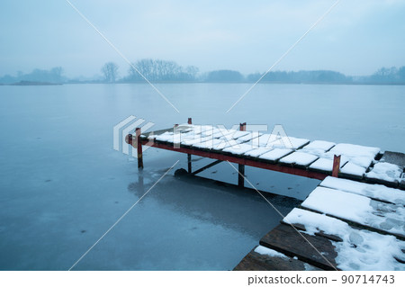 Snow on a pier on a frozen lake 90714743