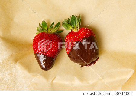 two fresh strawberries in chocolate on baking paper. delicious. two fresh strawberries in chocolate on baking paper. delicious. 90715003