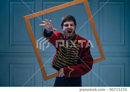 Creative portrait of young shouting man in image of medieval hussar posing isolated on dark blue background. Retro style, comparison of eras concept. 90715250