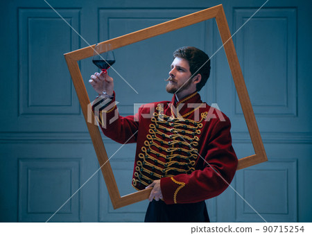 Creative portrait of young man in image of medieval hussar posing isolated on dark blue background. Retro style, comparison of eras concept. Creative portrait of young man in image of medieval hussar posing isolated on dark blue background. Retro style, comparison of eras concept. 90715254