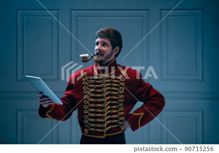 Creative portrait of young man in image of medieval hussar posing isolated on dark blue background. Retro style, comparison of eras concept. Creative portrait of young man in image of medieval hussar posing isolated on dark blue background. Retro style, comparison of eras concept. 90715256