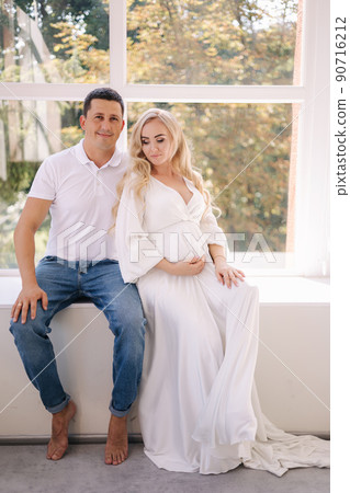 Happy future parents of man and pregnant woman puts hands on belly and waiting for beby movement in the belly. Studio photosession. Background of big mirror 90716212