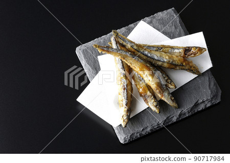 A bird's-eye view of fried silver-stripe round herring on a slate plate and top paper with a black background 90717984