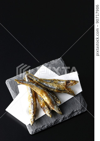 A bird's-eye view of fried silver-stripe round herring on a slate plate and top paper with a black background 90717986