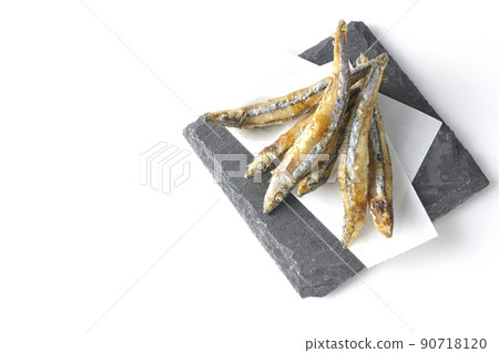 A bird's-eye view of fried silver-stripe round herring on a slate plate and top paper on a white background 90718120