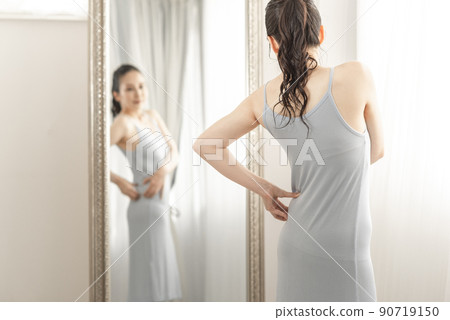 A woman who cares about her body shape while looking in the mirror 90719150