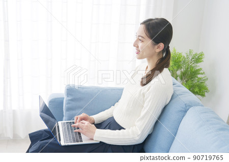 A woman sitting on the sofa and using a laptop 90719765