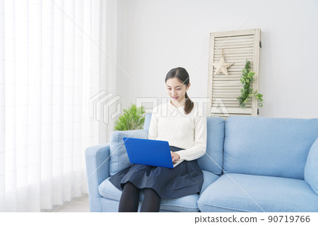 A woman sitting on the sofa in the living room and using a laptop 90719766