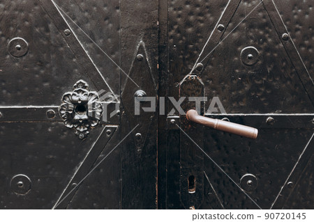 The handle on the metal door in the old style. Detail of medieval black door with metal decoration, abstract background, closeup 90720145