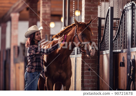 Good looking girl combs a paint horse inside a well-maintained stable Good looking girl combs a paint horse inside a well-maintained stable 90721678