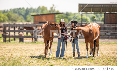 Two cowgirls meet their paint horses on a ranch on a sunny day Two cowgirls meet their paint horses on a ranch on a sunny day 90721740