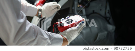 Mechanics hand using multimeter to measure voltage of car battery 90722739
