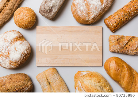 Minimalist wooden cutting board blank mockup on background of Types of homemade bread. Different kinds of fresh bread as background, top view with space for your text or design 90723990