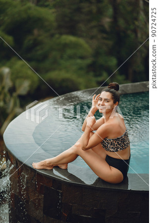 Woman sititng by the swimming pool. Lady in a swimsuit. Girl relaxing by the pool at a beach club in Bali Indonesia Woman sititng by the swimming pool. Lady in a swimsuit. Girl relaxing by the pool at a beach club in Bali Indonesia 90724725