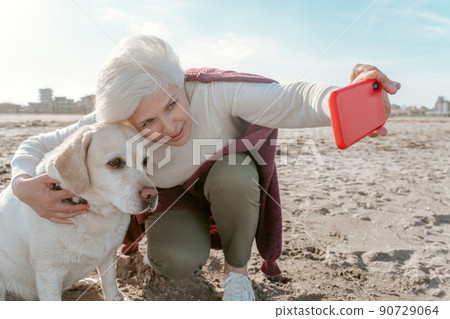 Lady photographing herself and the dog on the beach Lady photographing herself and the dog on the beach 90729064