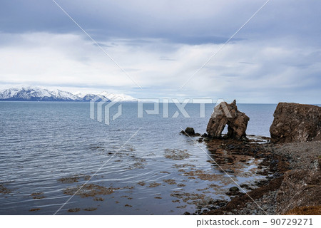 Rock formations at seashore with snowcapped mountain in background against sky 90729271
