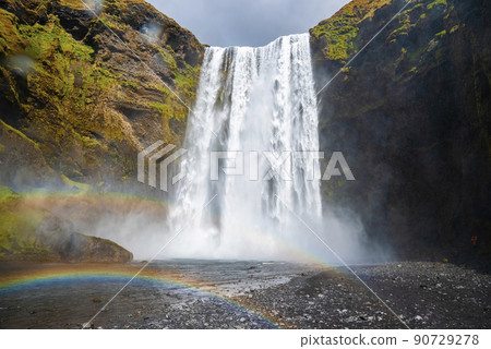 Low angle view of beautiful rainbows and Skogafoss waterfall falling from cliffs 90729278