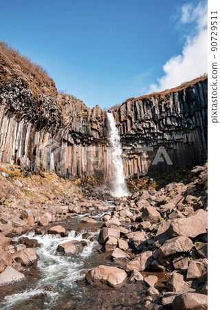 Beautiful cascades of Svartifoss waterfall and flowing stream against blue sky Beautiful cascades of Svartifoss waterfall and flowing stream against blue sky 90729511
