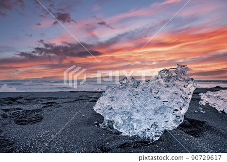 Beautiful ice crystal on black sand of Diamond beach against cloudy sky at sunset Beautiful ice crystal on black sand of Diamond beach against cloudy sky at sunset 90729617