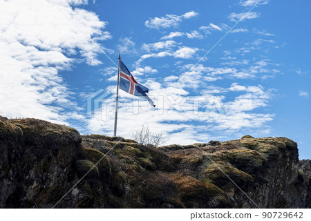 Icelandic flag waving on rocky cliff against blue cloudy sky Icelandic flag waving on rocky cliff against blue cloudy sky 90729642
