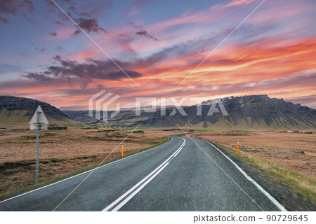 Empty highway leading towards mountain range against cloudy sky during sunset Empty highway leading towards mountain range against cloudy sky during sunset 90729645