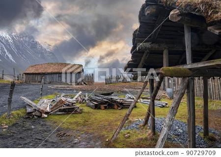Logs by shed and traditional houses surrounded by fence in old Viking village 90729709