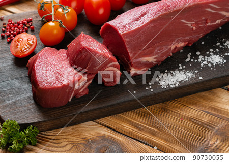 Slices raw meat fillet on wooden board 90730055