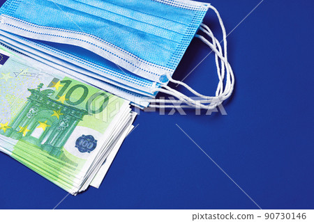 Pile of medical face masks and Euro banknotes on blue background Pile of medical face masks and Euro banknotes on blue background 90730146