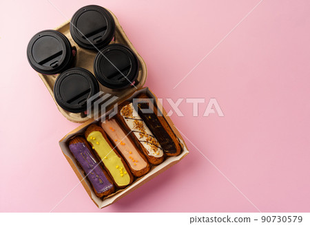 Box of eclairs with takeaway coffee cups on pink background Box of eclairs with takeaway coffee cups on pink background 90730579