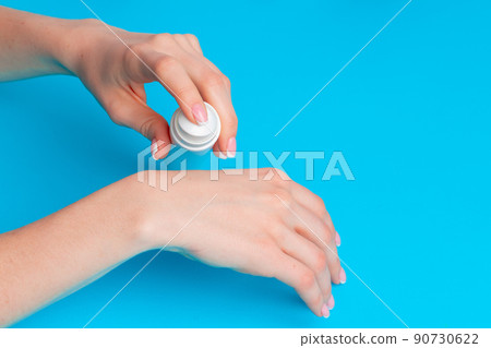 Female hand holding skincare product bottle on blue 90730622
