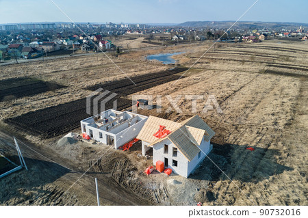 Aerial view of unfinished frame of private house with aerated lightweight concrete walls and wooden roof frame under construction. Aerial view of unfinished frame of private house with aerated lightweight concrete walls and wooden roof frame under construction. 90732016