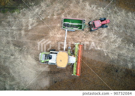 Aerial view of combine harvester unloading grain in cargo trailer working during harvesting season on large ripe wheat field. Agriculture and transportation of raw farm products concept Aerial view of combine harvester unloading grain in cargo trailer working during harvesting season on large ripe wheat field. Agriculture and transportation of raw farm products concept 90732084