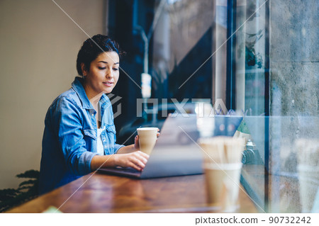 Skilled hipster girl with coffee to go using netbook for social networking and chatting 90732242