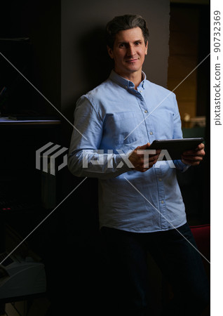 Portrait of confident businessman, successful entrepreneur, real estate agent, fashion designer, creative person with tablet posing in low light office, looking at camera 90732369