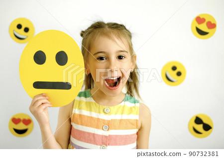 Naughty laughing girl with a sad disappointed smile face emoticon in her hand. World smile face Naughty laughing girl with a sad disappointed smile face emoticon in her hand. World smile face 90732381