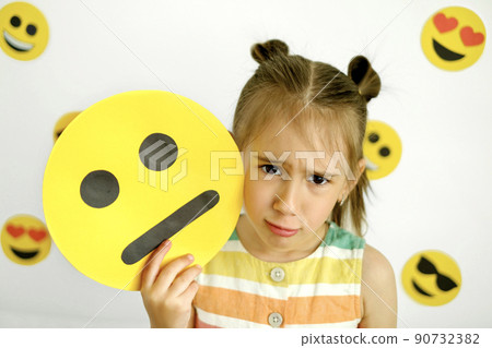 Sad upset girl pouting looks at the camera holding a carton saddened emoticon. Various emojis on a white background Sad upset girl pouting looks at the camera holding a carton saddened emoticon. Various emojis on a white background 90732382