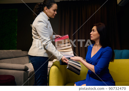 African woman interior designer in furniture design studio showing upholstery swatches of color fabrics of different qualities and textures to customer sitting on couch African woman interior designer in furniture design studio showing upholstery swatches of color fabrics of different qualities and textures to customer sitting on couch 90732470
