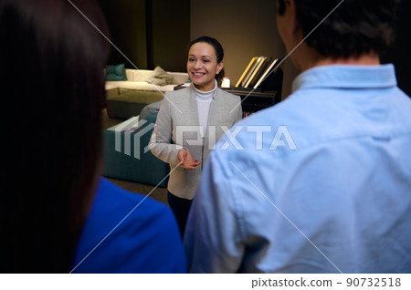 View through customers shoulders to a charming African woman sales representative consulting in a furniture design store 90732518