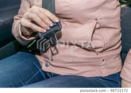 Close-up of a female passenger's hands trying to fasten their seat belt in a modern car. Close-up of a female passenger's hands trying to fasten their seat belt in a modern car. 90733172