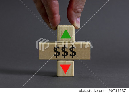 Dollar rates symbol. Businessman holds a wooden cube with arrow symbolizing that dollar rates are going down or up. Beautiful grey table grey background. Business and dollar rates concept. Copy space. 90733387