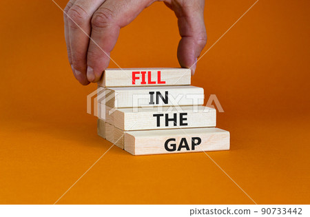 Fill in the gap symbol. Concept words Fill in the gap on wooden blocks on a beautiful orange table orange background. Businessman hand. Business, motivational and fill in the gap concept. 90733442