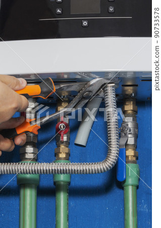 Plumber attaches to pipe gas boiler using adjustable wrench. Plumber attaches to pipe gas boiler using adjustable wrench. 90733578