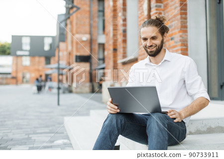 Handsome caucasian man in stylish wear sitting on stairs and working on wireless laptop. 90733911