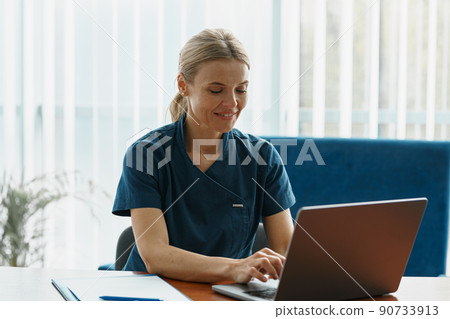 Smiling doctor therapist working laptop during appointment in her medical office  90733913