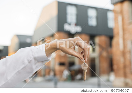 Woman hand holds the keys to an apartment against the background of buildings. Woman hand holds the keys to an apartment against the background of buildings. 90734097